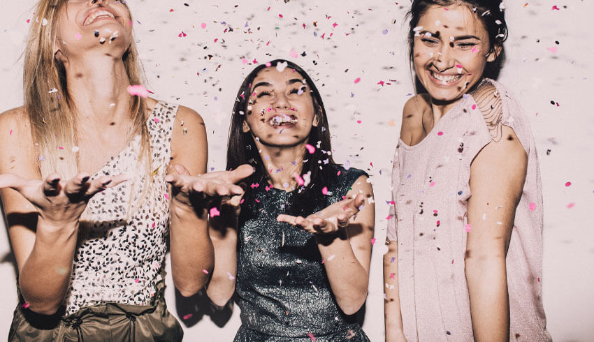 Three women smile as they throw confetti in the air